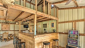 Un coin bar au style rustique, avec des tabourets de bar en bois, un vieux juke-box et un plafond haut aux poutres apparentes.