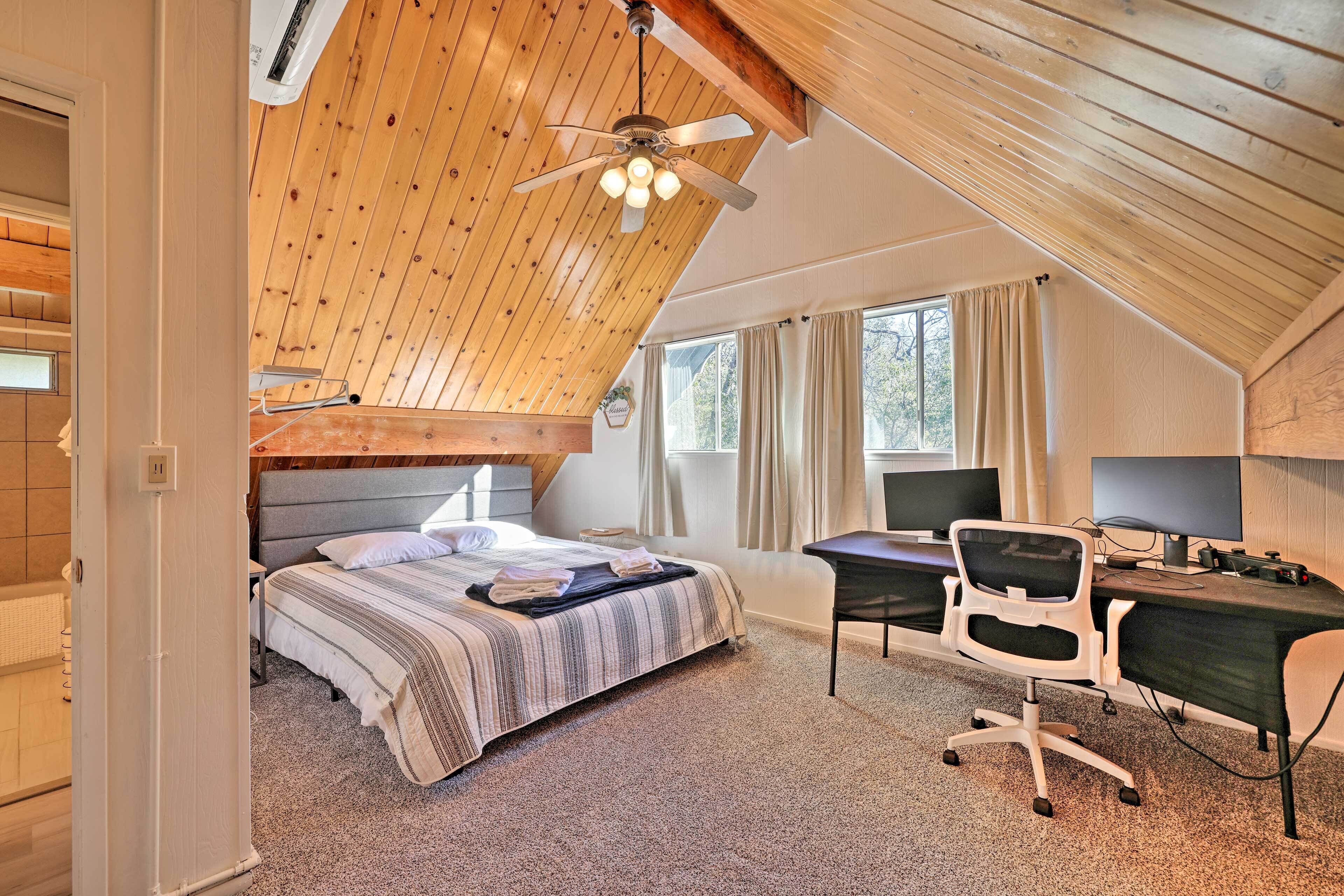 A bedroom with a sloped ceiling, a bed with a striped bedspread, a desk with a computer, and a chair.