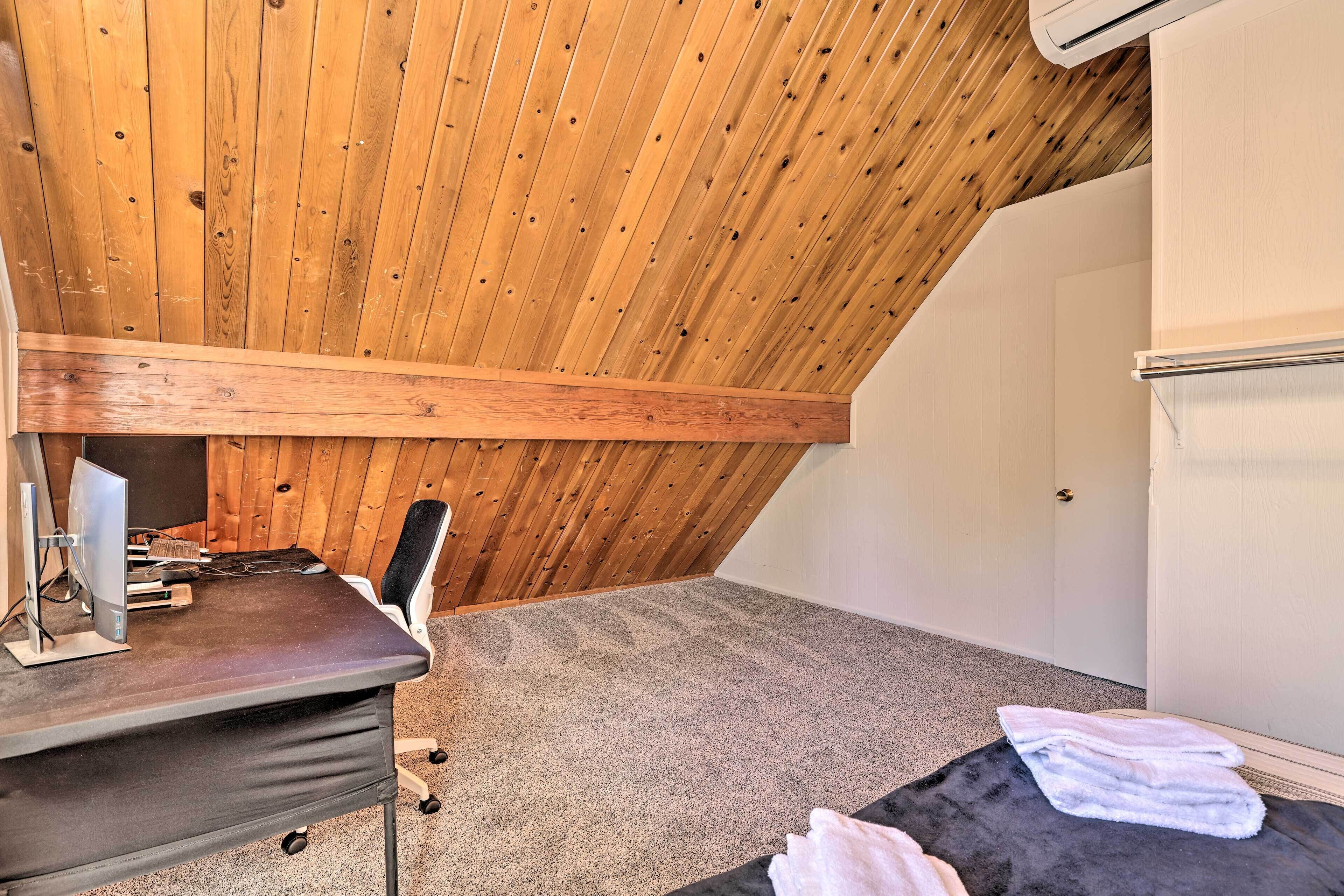 Une petite pièce avec un toit en pente, comprenant un bureau, une chaise et un ordinateur.