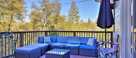 A deck with a blue sofa, wicker ottoman, and a folding chair.