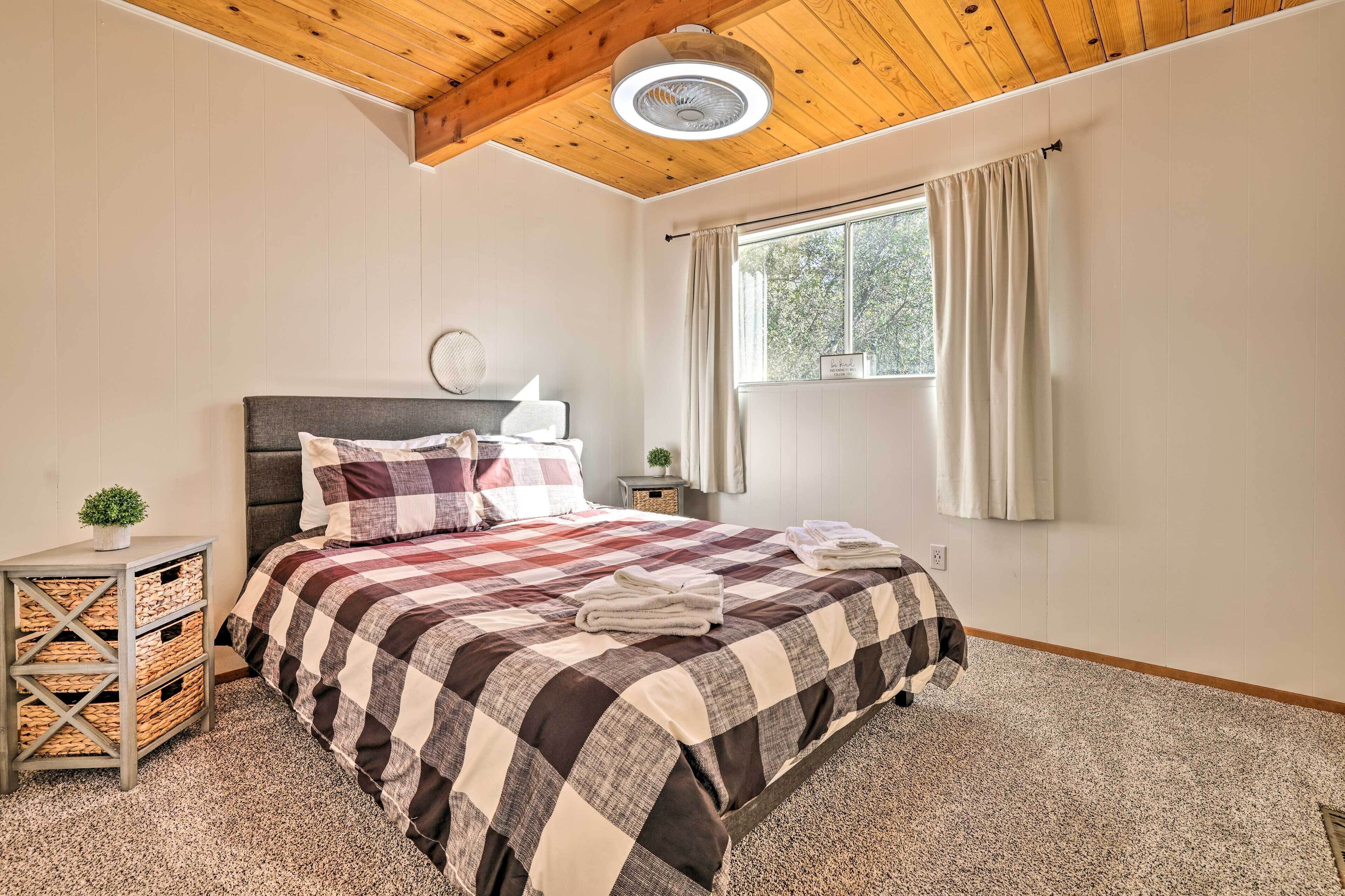 Een slaapkamer met een geruite spreideken, houten balken in het plafond, een nachtkastje met een lamp en een raam met gordijnen.