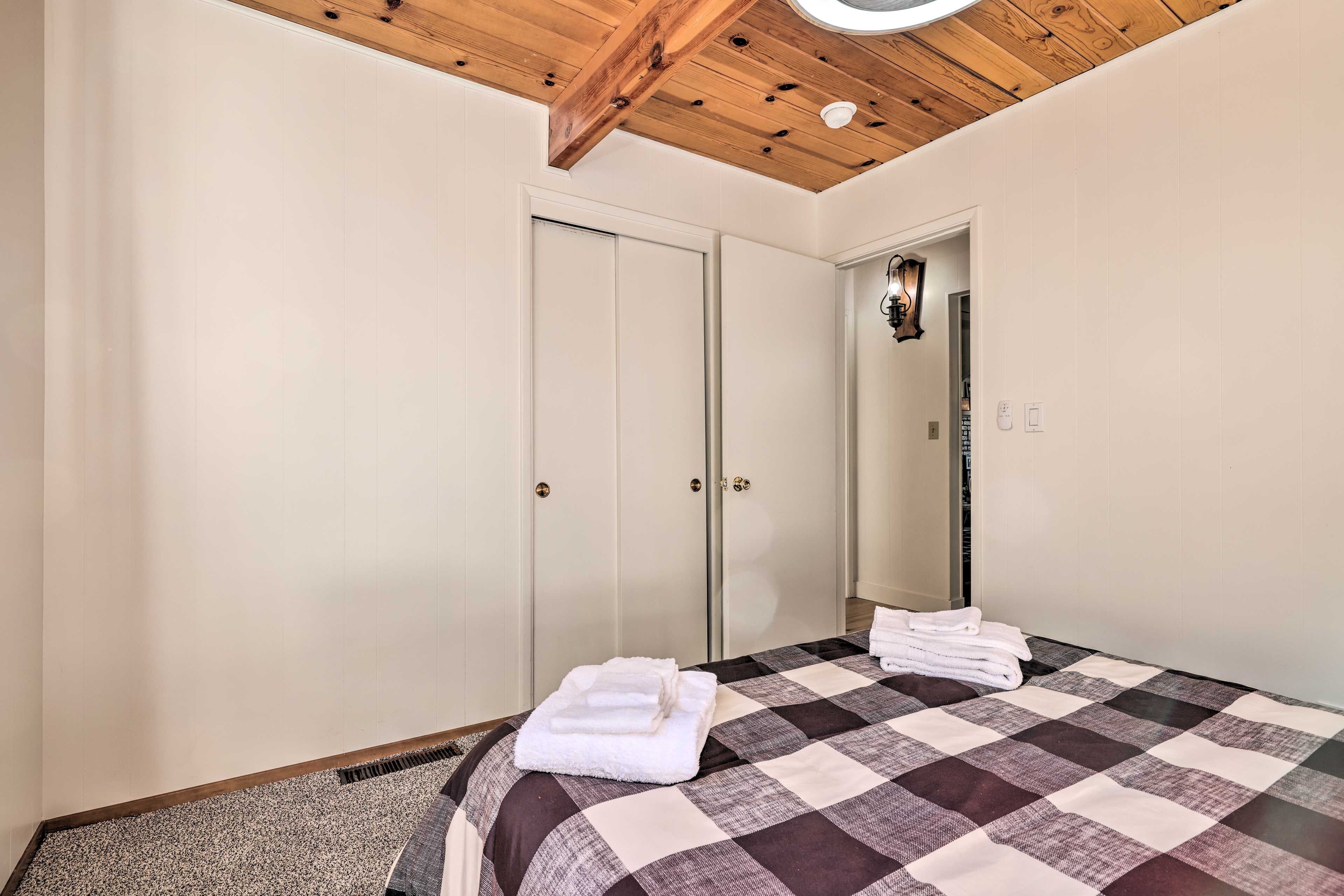 A bedroom with a checkered bedspread, two white doors, a wooden ceiling, and a mirror on the wall.