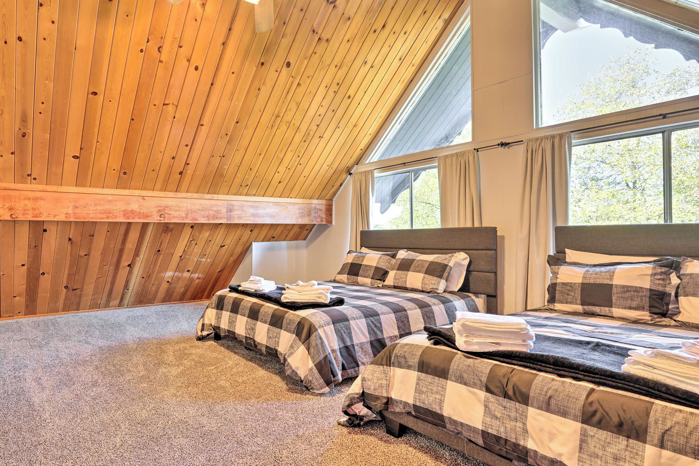 A bedroom with two beds, wooden ceiling beams, large windows, and a carpeted floor.