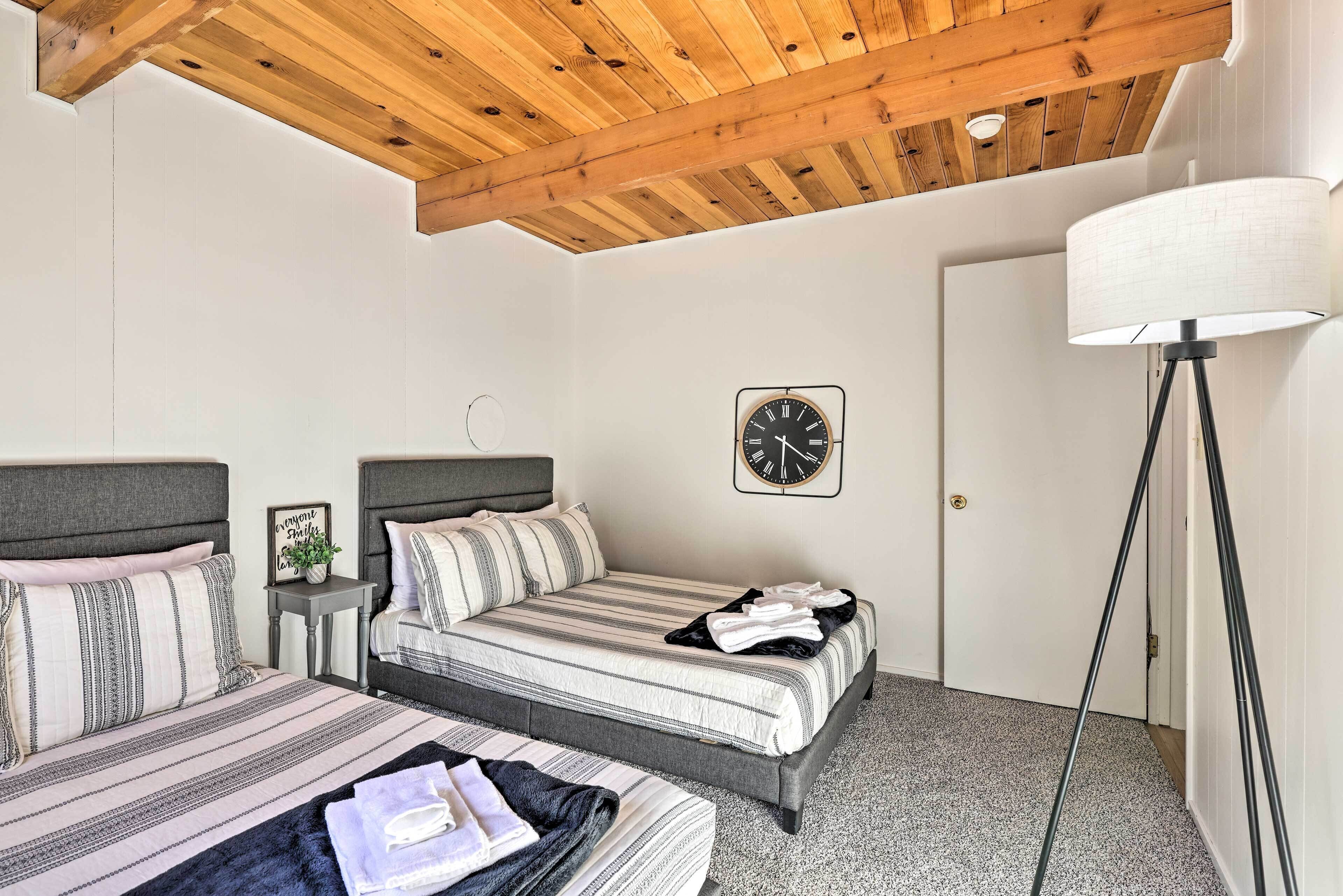 A bedroom with two beds, a wooden ceiling, a clock, a lamp, and a small table with a plant.