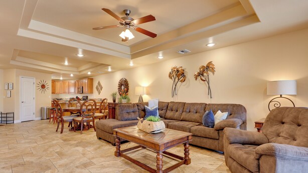 A spacious living room with a large brown sofa, a wooden coffee table, and a dining area with wooden chairs and a table. - Step-free Bullhead City Condo w/ Balcony! (Bullhead City)