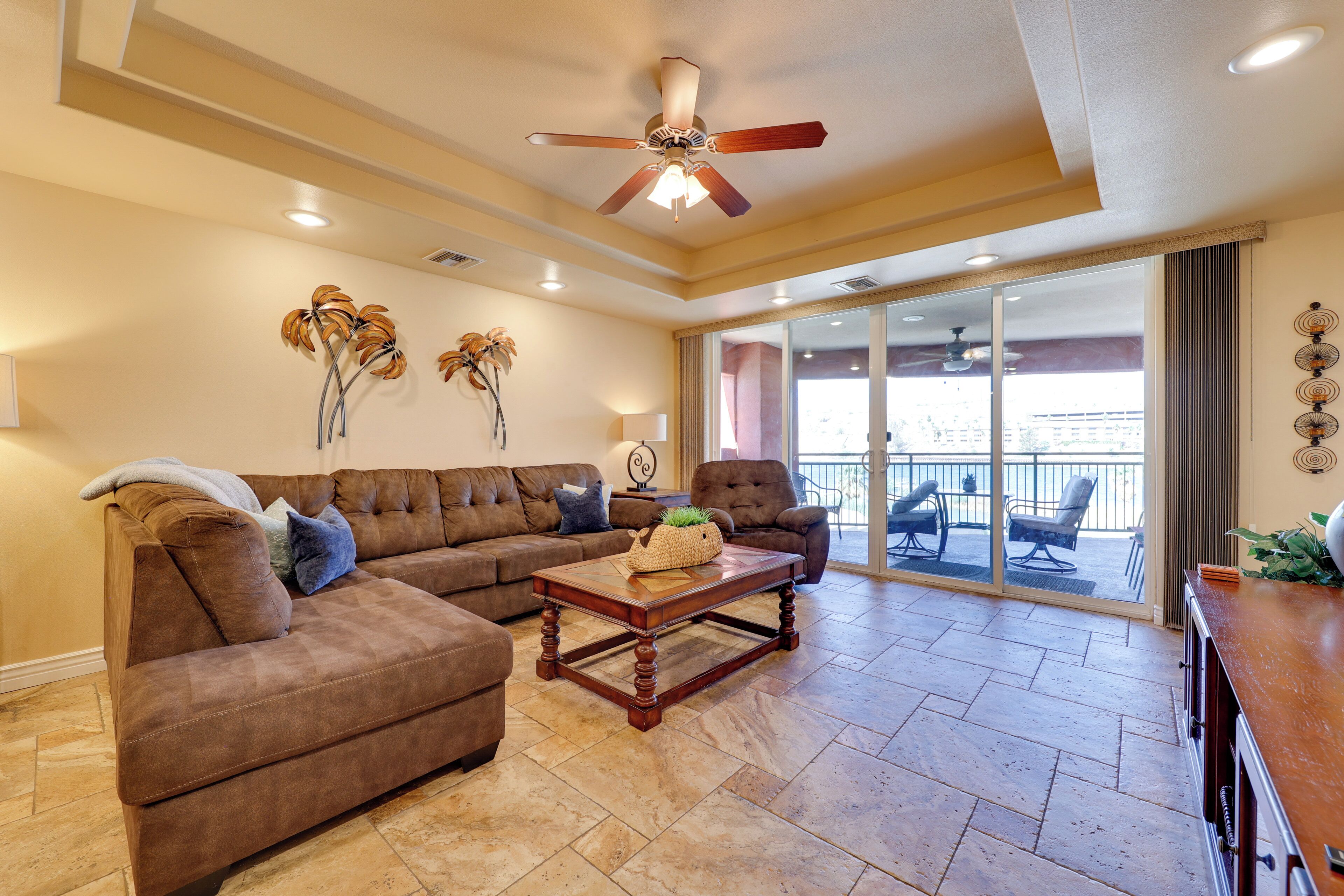 A spacious living room with a brown sectional sofa, a wooden coffee table, and a ceiling fan.