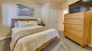 Een slaapkamer met een bed, een houten dressoir, een plafondventilator en een kunstwerk aan de muur.