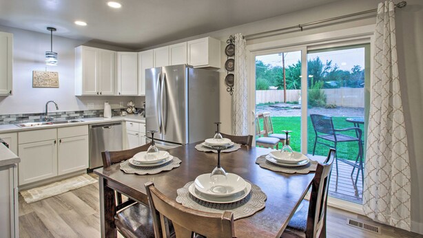 A modern kitchen with white cabinets, stainless steel appliances, and a dining area with a wooden table set for four. - 1 Mi to Winery: Clifton Escape w/ Grill & Yard! (Clifton)