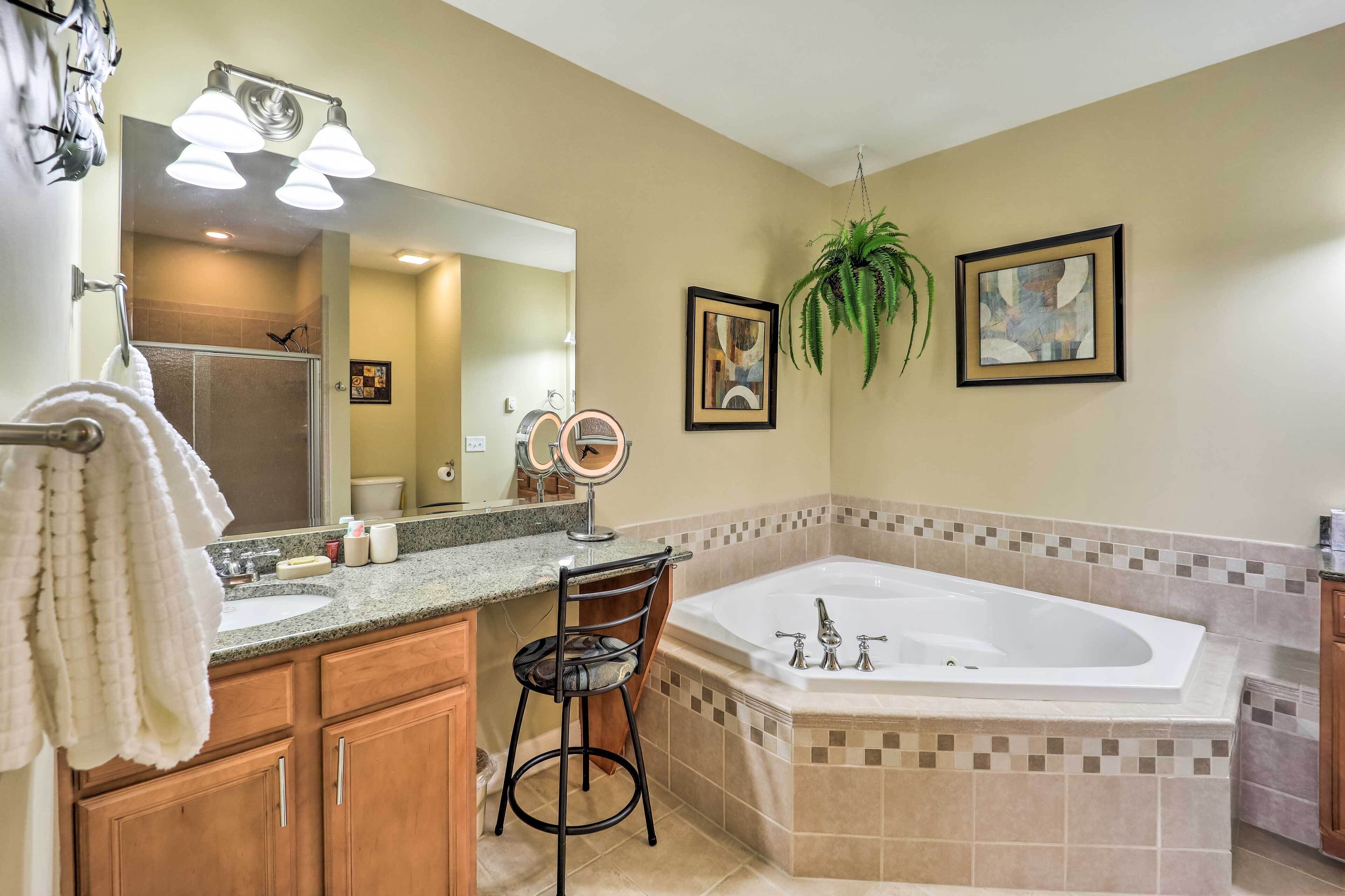 A bathroom with a large bathtub, a vanity with a mirror, and a hanging plant.