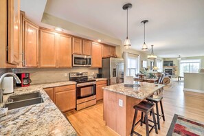 A spacious kitchen with wooden cabinets, stainless steel appliances, a granite countertop, and a central island with bar stools.