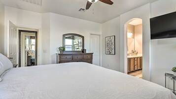 A bedroom with a large bed, a ceiling fan, a dresser, a mirror, and a TV mounted on the wall.