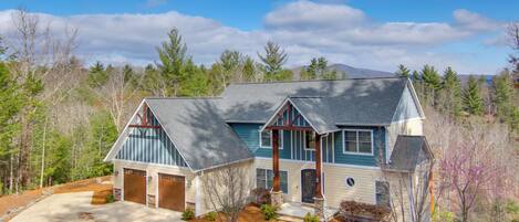 A two-story house with a stone foundation, a front porch, and a driveway leading to a garage.