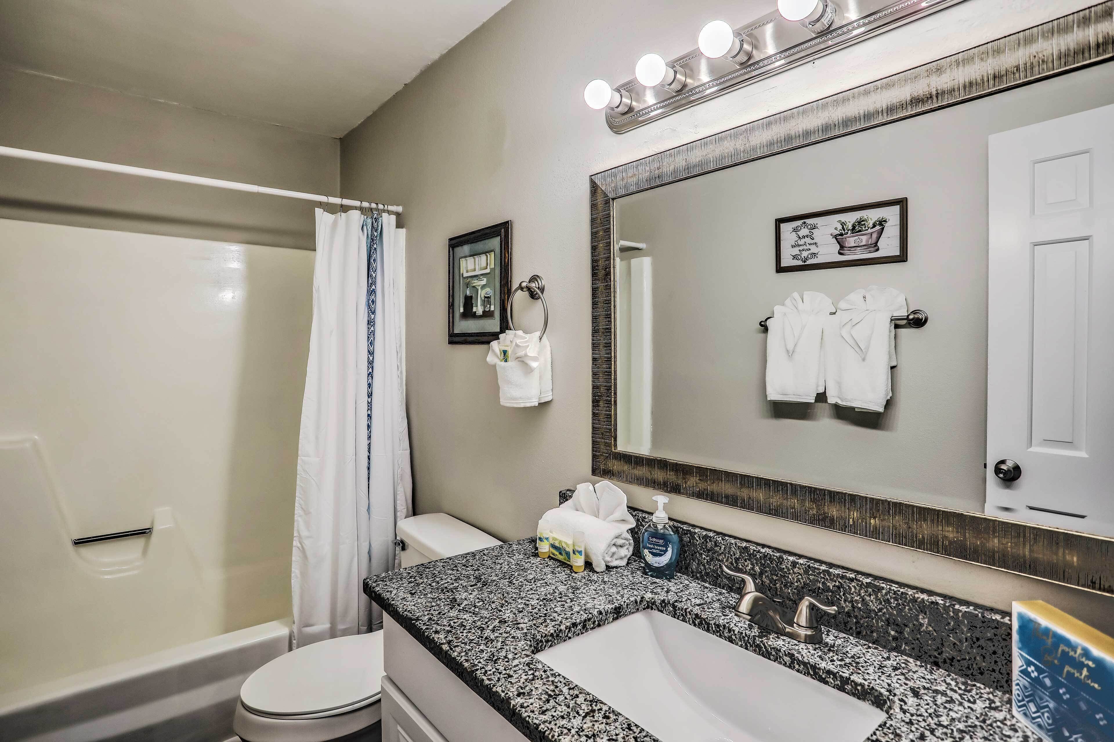 A bathroom with a shower, toilet, sink, and a large mirror with lights.