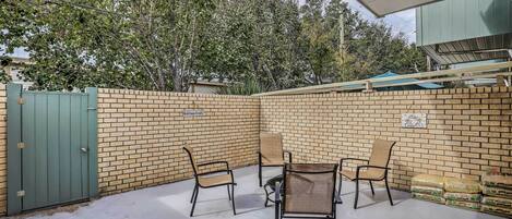 A covered patio area with a brick wall, a green gate, and outdoor furniture.