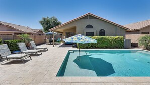 A swimming pool with lounge chairs and umbrellas, a covered patio, and a building with a tiled roof. - Sunny Maricopa Getaway w/ Private Pool + Fire Pit! (Maricopa)