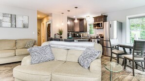 A living room with a beige sofa, a glass coffee table, and a dining area with a table and chairs. - 4 Mi to Main Street: Petite Weaverville Escape! (Weaverville)