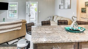 A modern kitchen with a granite countertop, a dining area with a table and chairs, and a living room with a sofa and a television. - 4 Mi to Main Street: Petite Weaverville Escape! (Weaverville)
