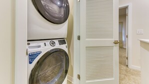 A laundry room with a front-loading washer and dryer, a door with louvered panels, and a carpeted floor. - Updated Charlotte Vacation Rental 4 Mi to Downtown (Charlotte)