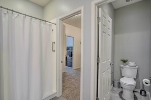 Un baño con inodoro, cortina de ducha y puerta que da a un cuarto de lavado.