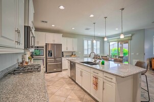 Una cocina moderna con gabinetes blancos, electrodomésticos de acero inoxidable, encimeras de granito e iluminación colgante.