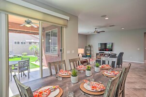 Un comedor con una mesa preparada para seis, un televisor al fondo y un patio con césped y sillas.