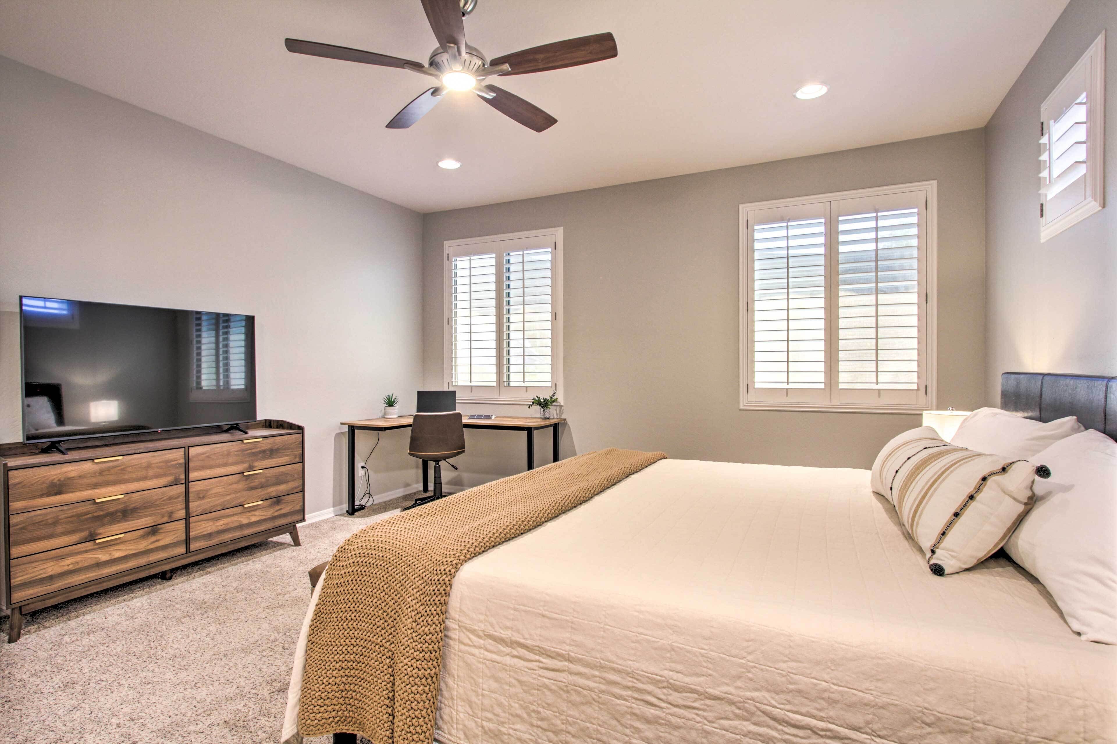 A bedroom with a bed, a TV, a desk, and a ceiling fan.