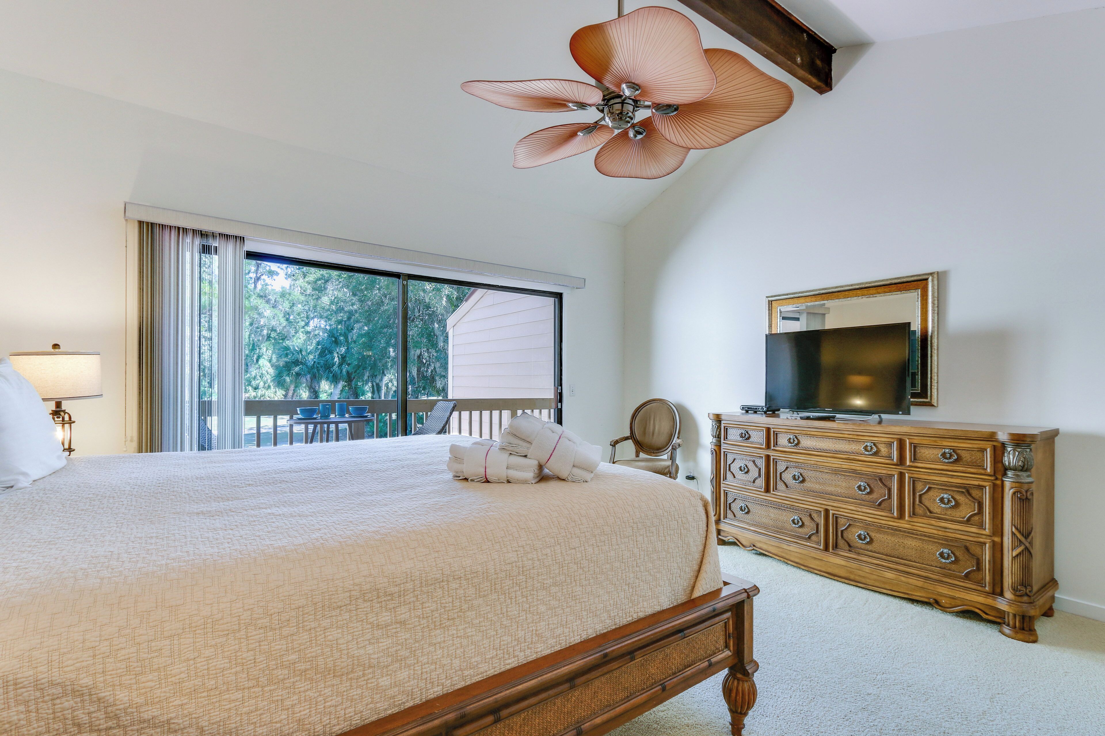 Une chambre à coucher avec un grand lit, une commode, un téléviseur et un ventilateur de plafond.