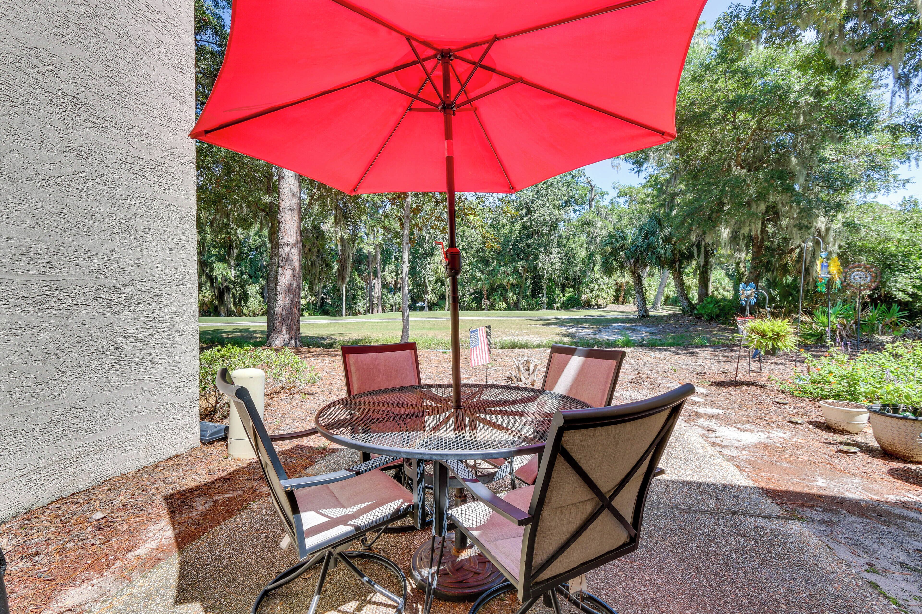 Une table ronde en métal, avec quatre chaises et un parasol rouge.