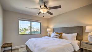 A bedroom with a large bed, a ceiling fan, a window with a view, and bedside lamps. - Putting Green, Community Perks: Sun City West Home (Sun City West)