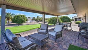 A covered patio with wicker furniture, a grill, and a view of a well-maintained lawn and neighboring houses. - Putting Green, Community Perks: Sun City West Home (Sun City West)