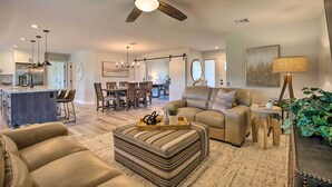 A spacious living room with a large sofa, ottoman, and a dining area in the background. - Putting Green, Community Perks: Sun City West Home (Sun City West)