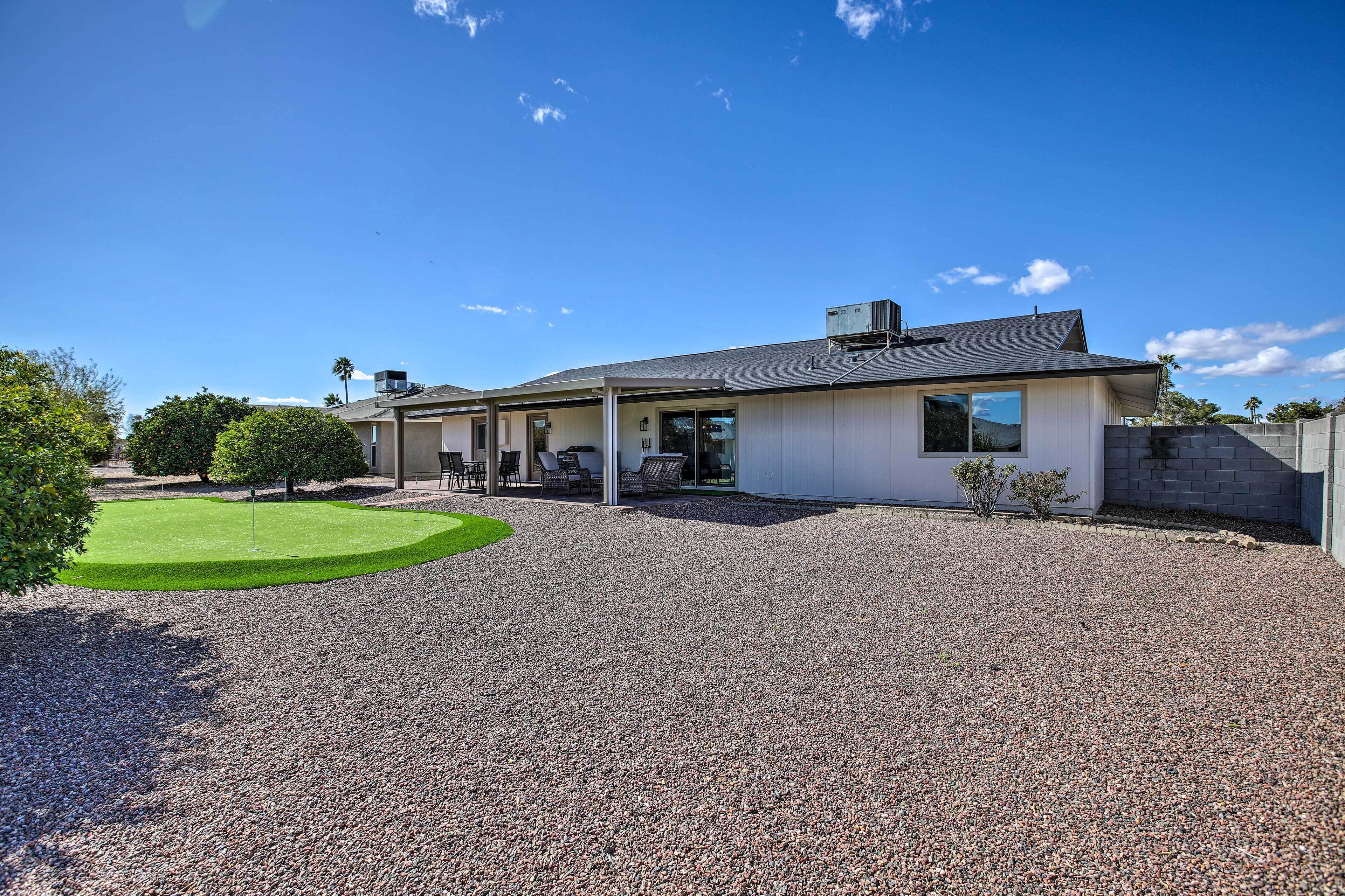 A modern house with a gravel driveway, a lawn, and a patio area with outdoor furniture.