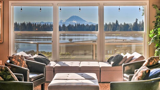 A living room with a large window overlooking a lake and a mountain. There are multiple seating options including a sofa and chairs. - Stunning Kent Lake House w/ Private Dock! (Covington)