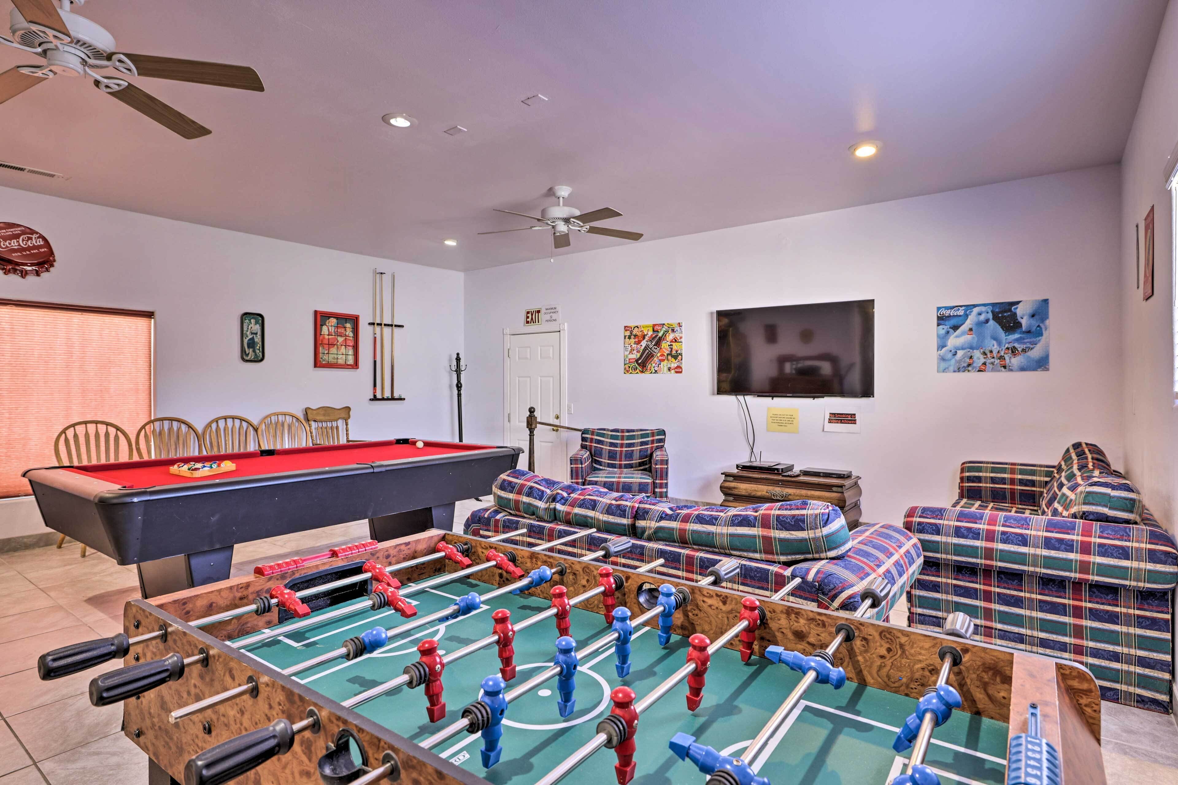 A room with a foosball table, a pool table, and a sofa set.