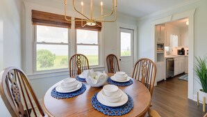 Comedor con una mesa de madera dispuesta para cuatro, un candelabro y ventanas amplias con vistas a la vegetación.
