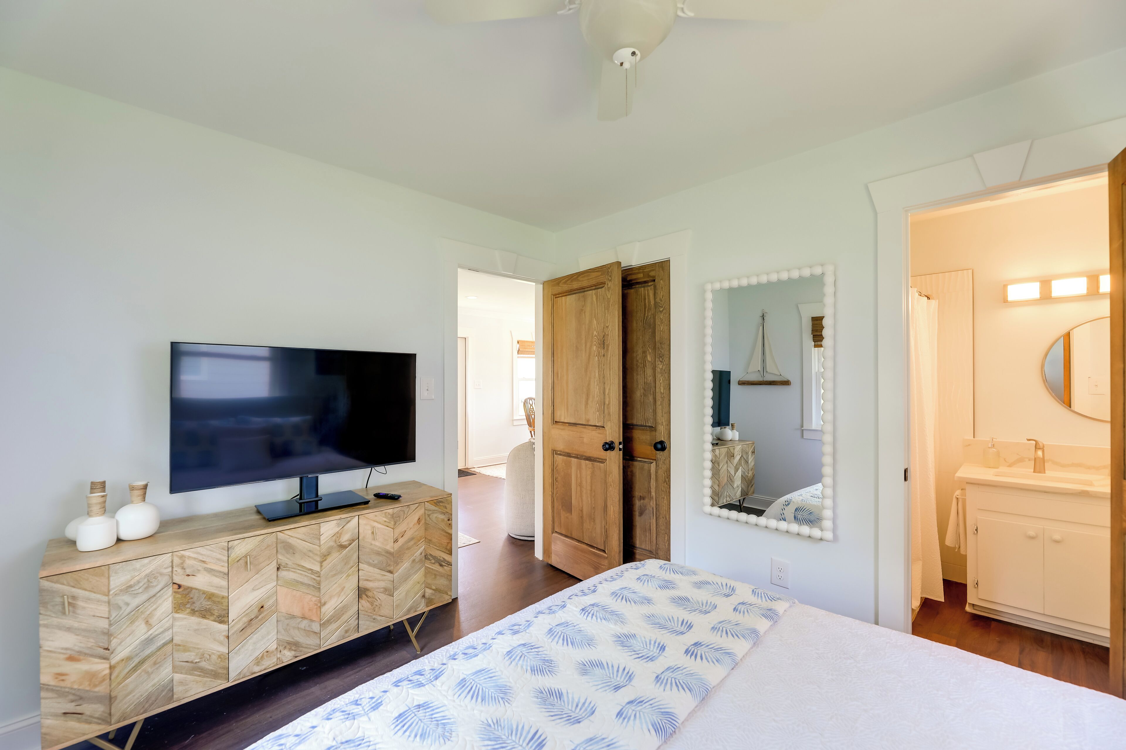 A bedroom with a bed, a TV on a wooden cabinet, a wooden wardrobe, and a bathroom with a mirror and sink.