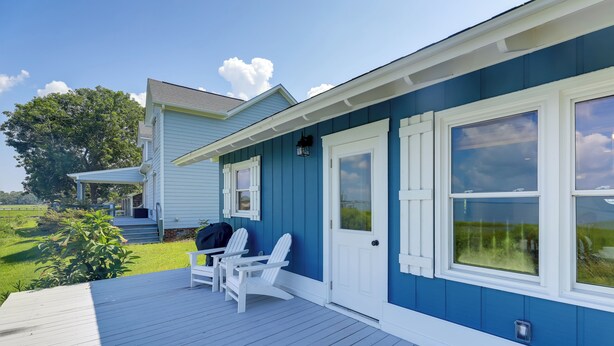 Una casa azul con porche, contraventanas blancas y una pequeña terraza con dos sillas Adirondack.
