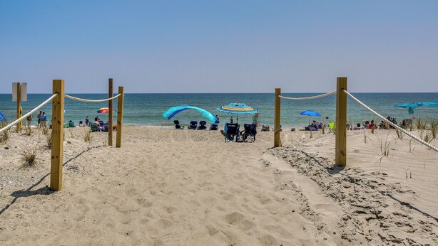 Ein sandiger Strand mit Holzbalken und Seilen, Sonnenschirmen und Menschen.