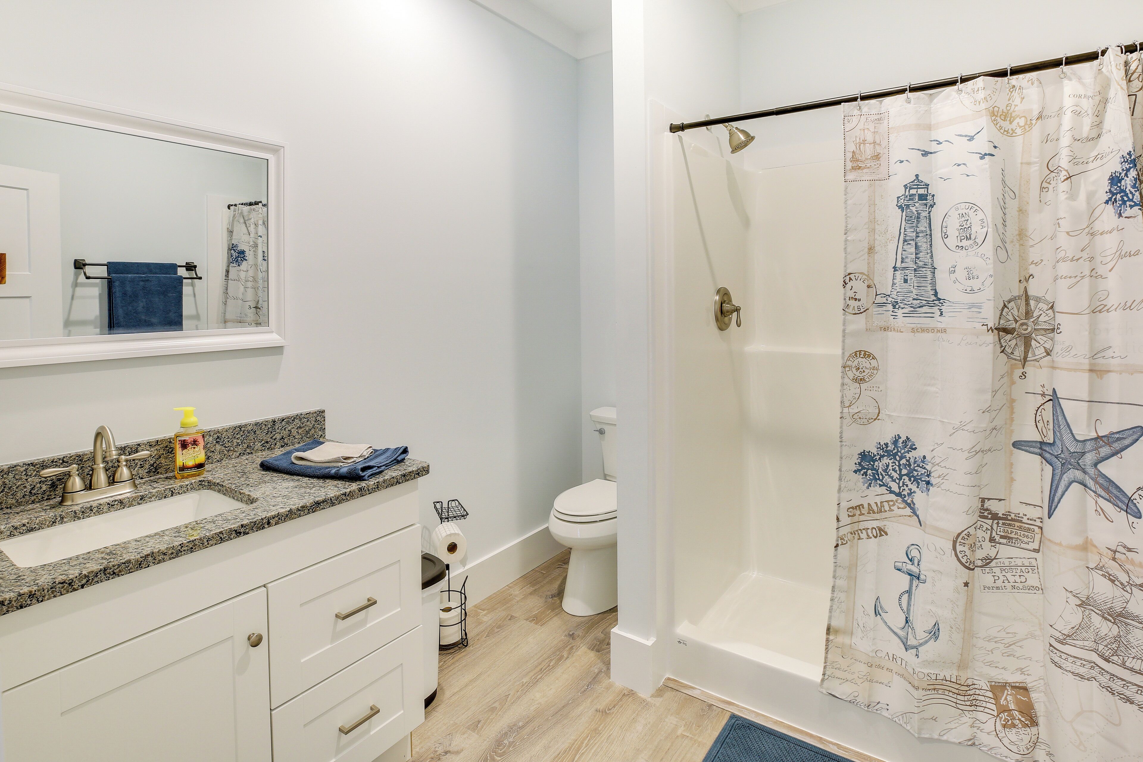 A bathroom with a shower curtain featuring maritime designs, a toilet, a sink with a faucet, and a mirror above the sink.