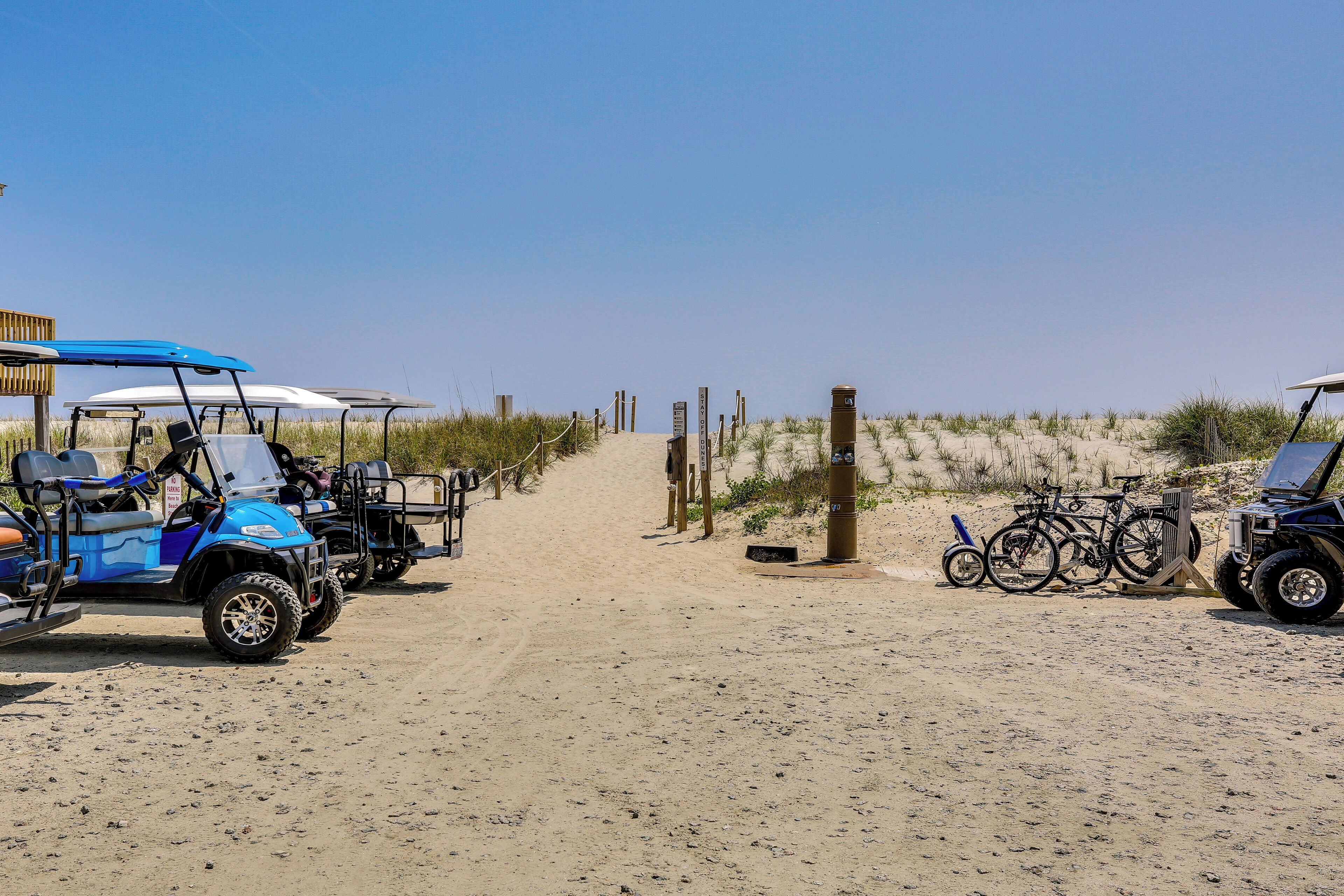 A sandy path leading to a beach area with golf carts and bicycles parked.