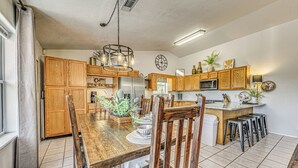 A kitchen with wooden cabinets, a stainless steel refrigerator, a wooden dining table with chairs, and a bar area with stools. - Charming Ruidoso House w/ Deck & Mountain Views! (Ruidoso)