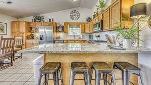 A kitchen with wooden cabinets, a marble countertop, and a clock on the wall. - Charming Ruidoso House w/ Deck & Mountain Views! (Ruidoso)