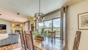 A dining area with a wooden table and chairs, a chandelier, and a large window with curtains. - Charming Ruidoso House w/ Deck & Mountain Views! (Ruidoso)