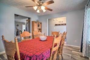 A dining room with a red patterned tablecloth, wooden chairs, a ceiling fan, and a kitchen in the background. - Charming 'hideaway Haven' Near Pigeon Forge! (Dandridge)