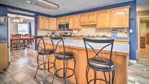 A kitchen with wooden cabinets, a central island with bar stools, and a dining area with a table and chairs. - Charming 'hideaway Haven' Near Pigeon Forge! (Dandridge)