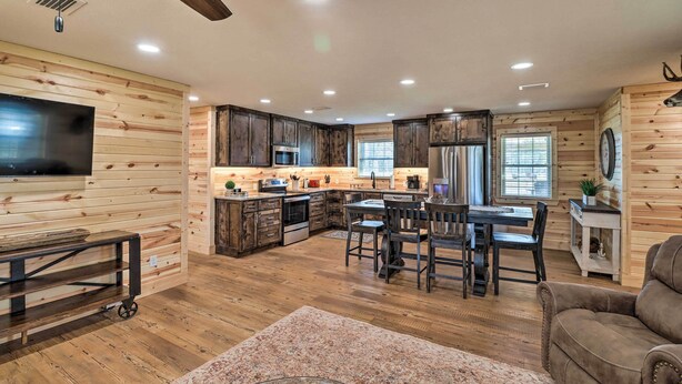 Una cocina amplia con armarios de madera, un comedor con mesa y sillas, y un televisor montado en la pared.