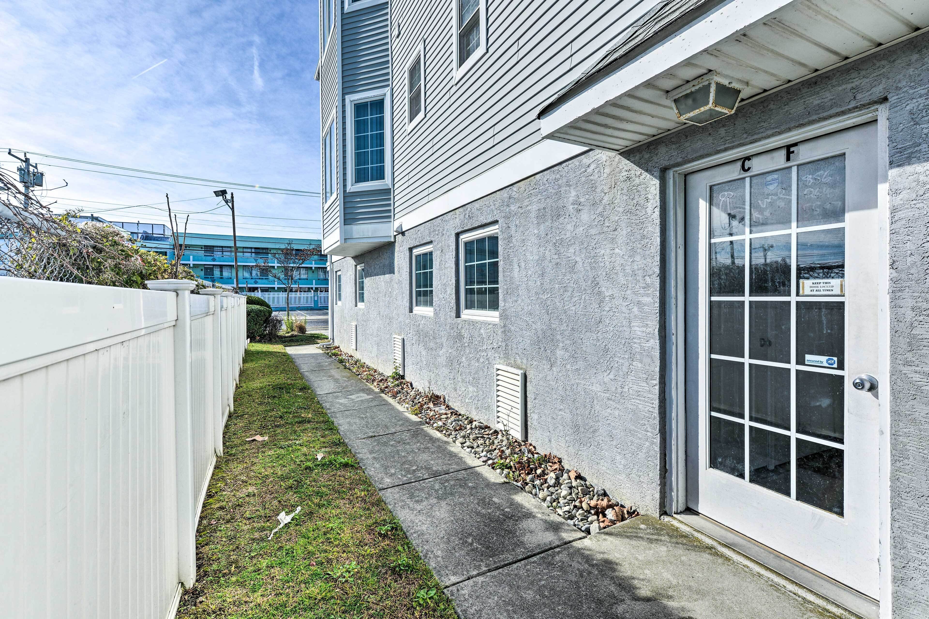 A building with a garage door, a concrete pathway, and a white fence.