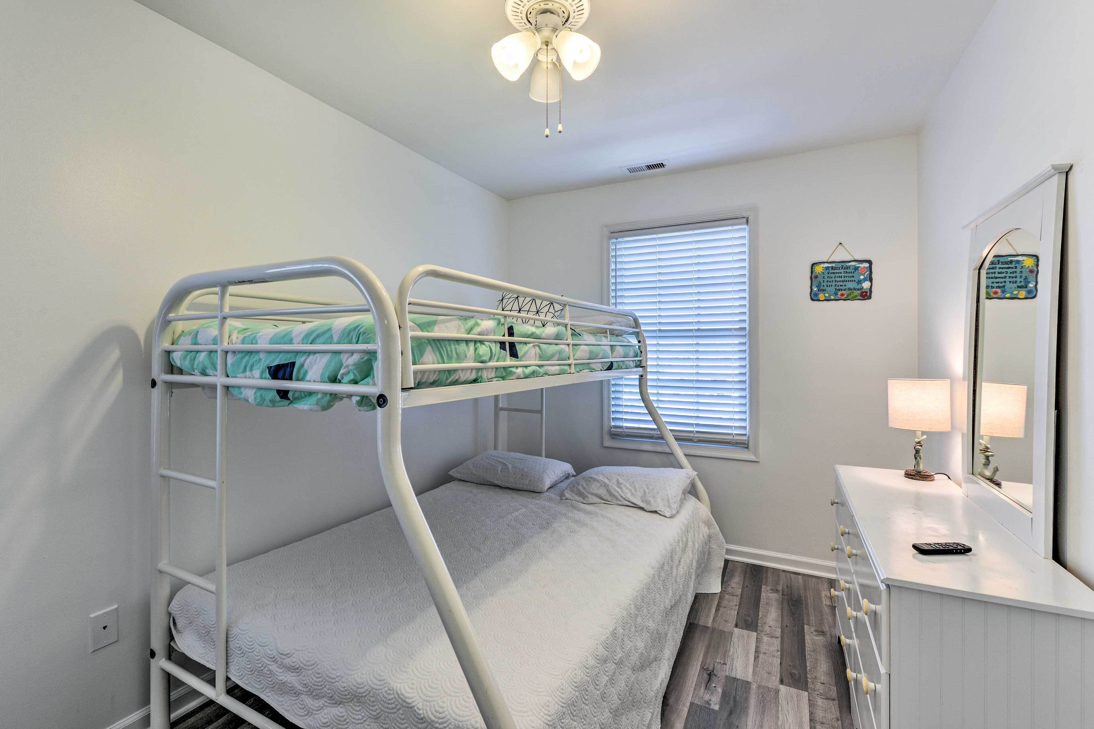 Un lit superposé avec une couvre-lit à motifs verts et blancs, une table de chevet avec une lampe et un miroir au-dessus.