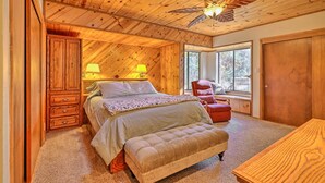 A bedroom with a wooden ceiling, a bed with a canopy, a bench, and a window with a view of trees.
