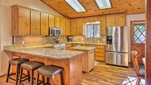 A kitchen with wooden cabinets, a central island with stools, stainless steel appliances, and skylights.